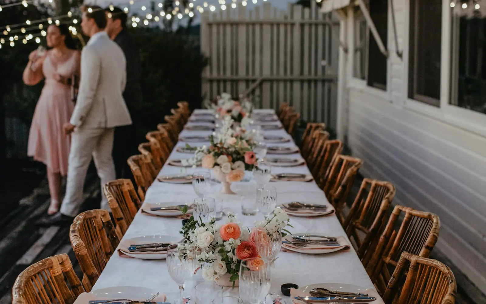 A couple beside a long outdoor wedding reception table under string lights