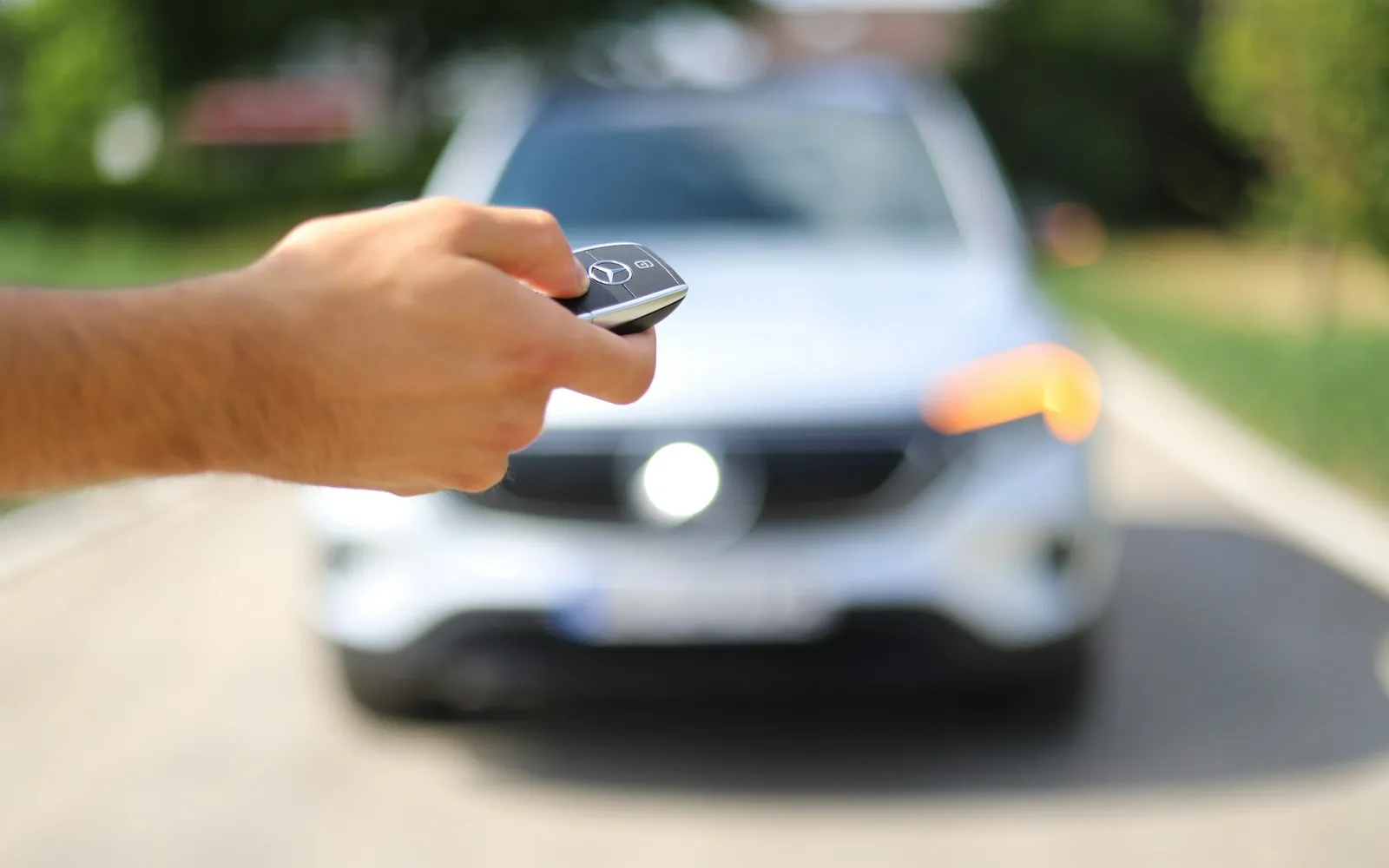 Hand holding a car key fob in front of a silver car