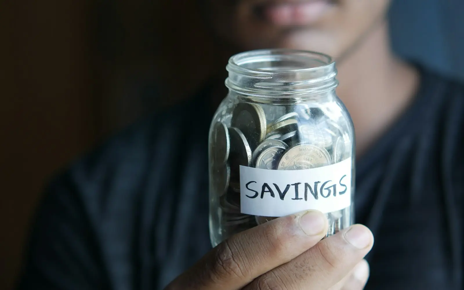 A person holding a glass jar of coins labeled savings