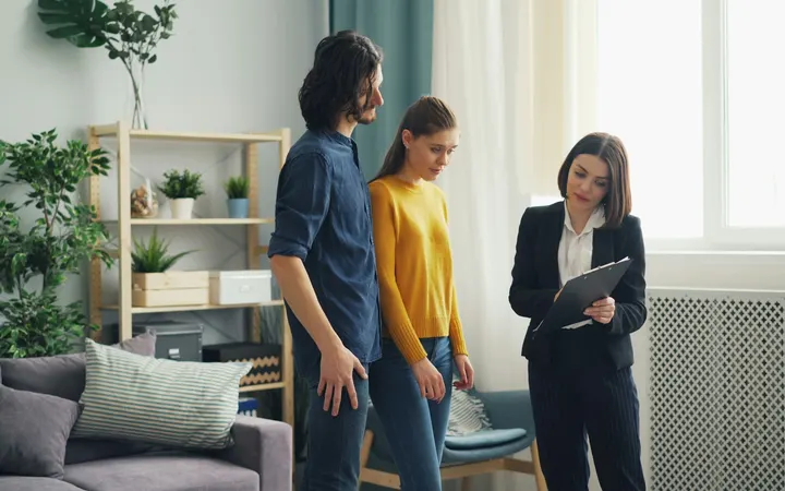 Home inspector with a clipboard talking to buyers in a living room
