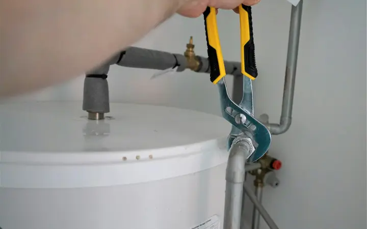 A plumber tightening a pipe fitting on top of a white tank water heater