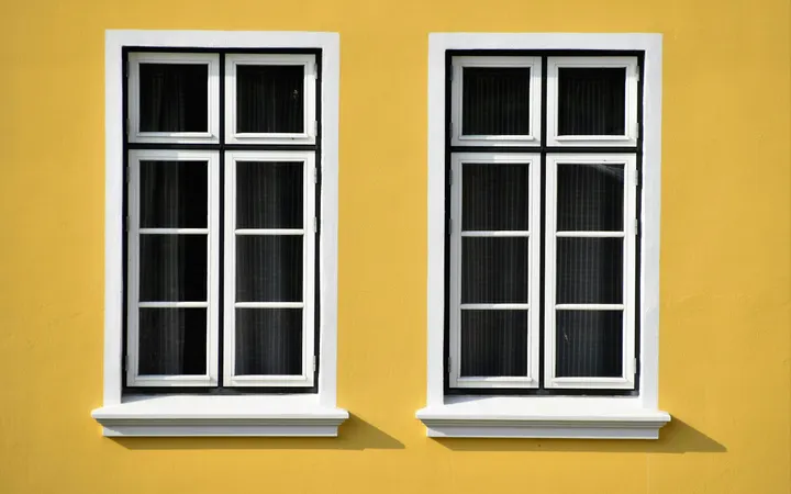 Two white wooden windows on a yellow wall